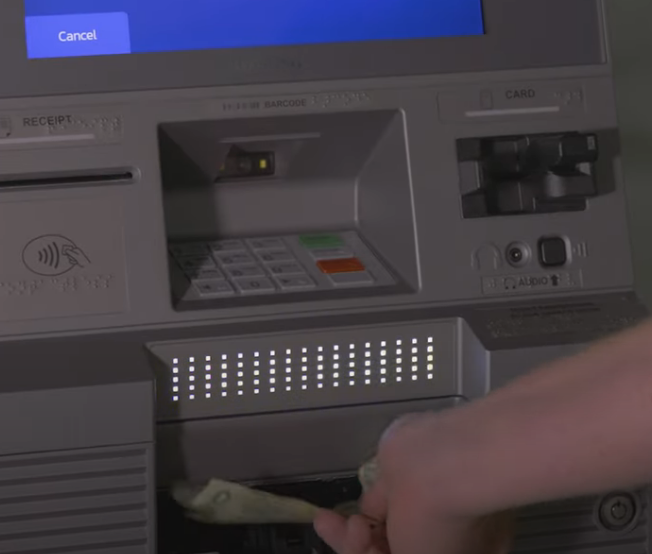 A person withdrawing cash from an ATM, with a blue Cancel button visible on the screen.