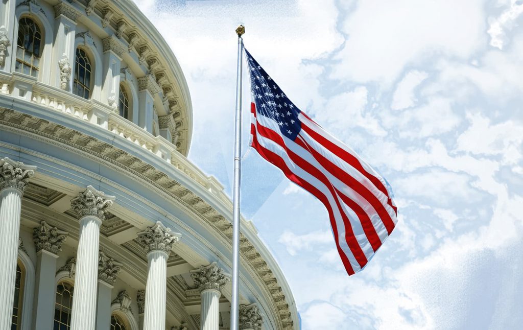 US flag waving in front of the Capitol building under a partly cloudy sky.