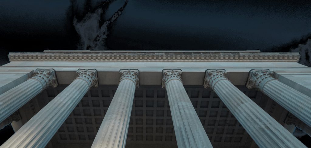 Low-angle view of tall marble columns and a decorated roof against a dark night sky.