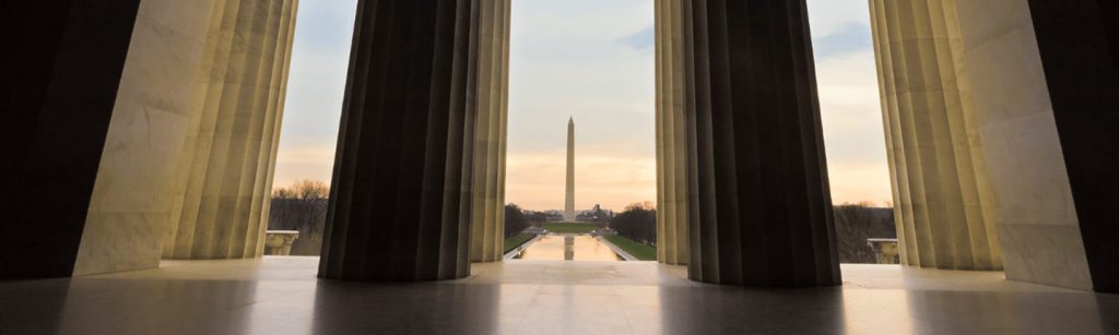 View of the Washington Monument at sunset, framed by the columns of the Lincoln Memorial.