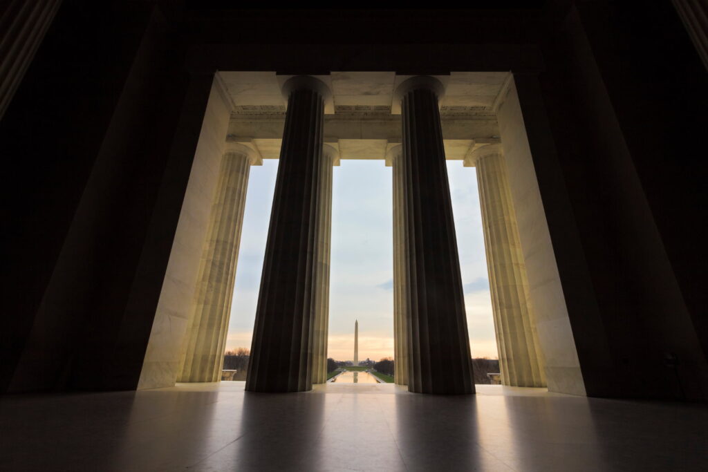 Three large columns frame a distant view of the Washington Monument at sunset.