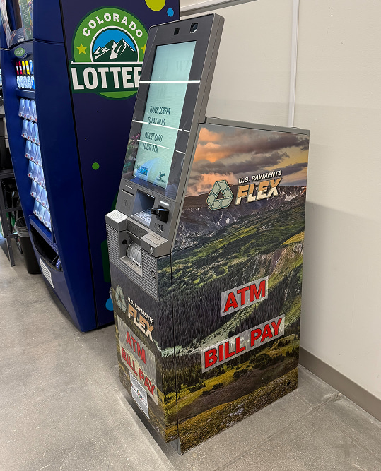 ATM and bill pay kiosk with mountain scenery design next to a Colorado Lottery vending machine.